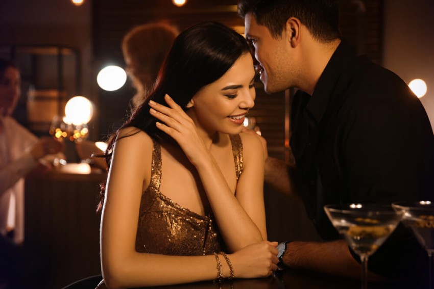 Heisses Sex Date Schweiz: Mann flüstert einer Frau in einer Bar intime Worte zu.