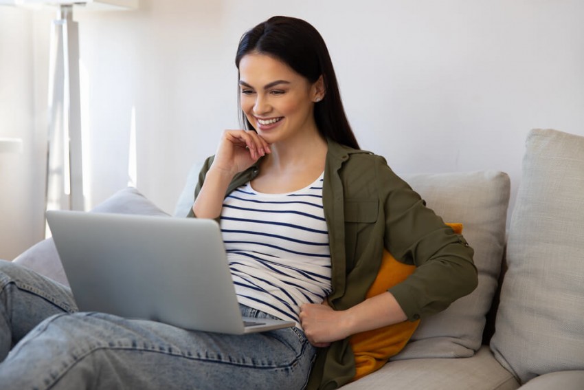 Lachende Frau beim diskreten Sexchat online über Laptop auf der Couch.